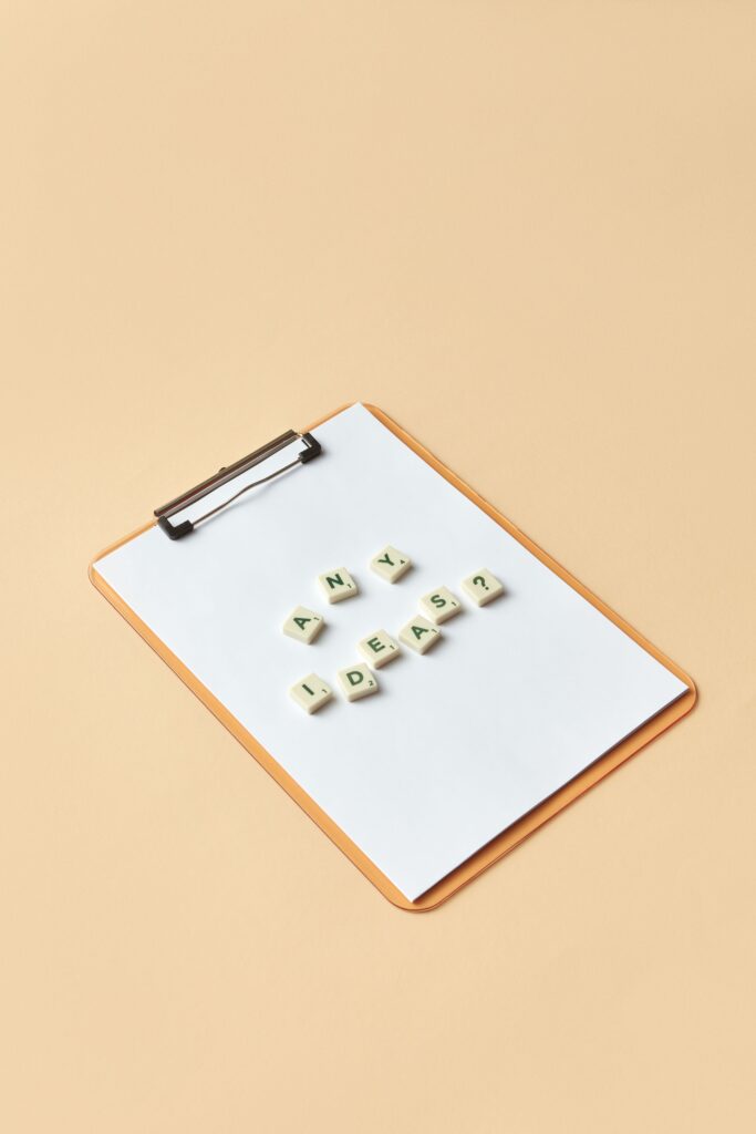 A minimalist flat lay of a clipboard with letter tiles spelling 'Any Ideas?' for creative inspiration.