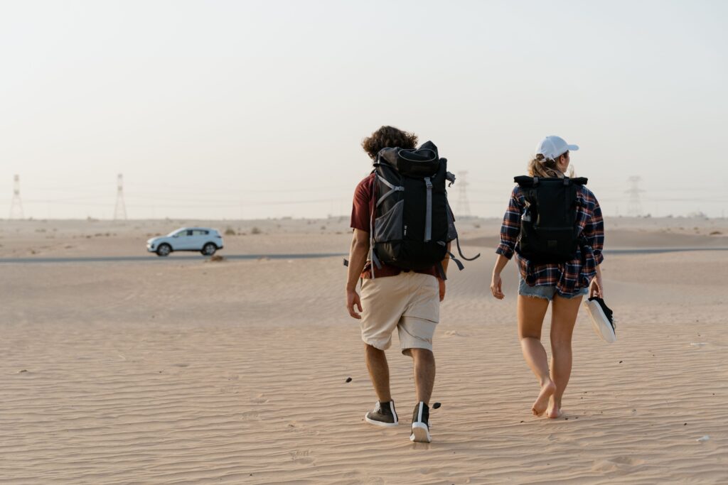 A couple walking in a vast desert with backpacks, heading towards the horizon.